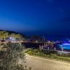 Vista notturna di una piscina illuminata e giardini.