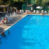 Piscina con lettini e persone sedute, immersa in un ambiente verde.
