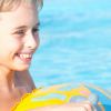 Bambino sorridente in piscina con un galleggiante colorato.