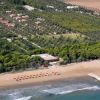 Veduta aerea di spiaggia, ombrelloni, villette tra alberi e campi.