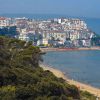 Vista su una spiaggia con città collinare e bagnanti in acqua.
